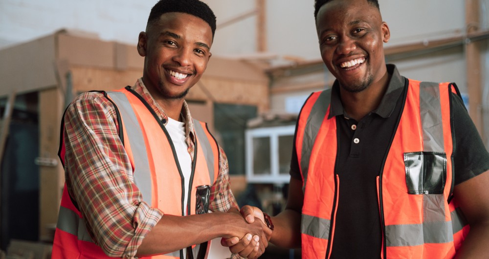 Un jeune apprenti et son maître d'apprentissage se serrent la main sur un chantier, symbolisant la signature d'un contrat d'apprentissage avec la CMA IDF.