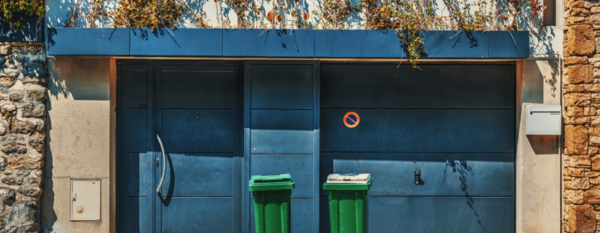Maison de ville avec une porte et une porte de garage bleues et 2 poubelles vertes devant
