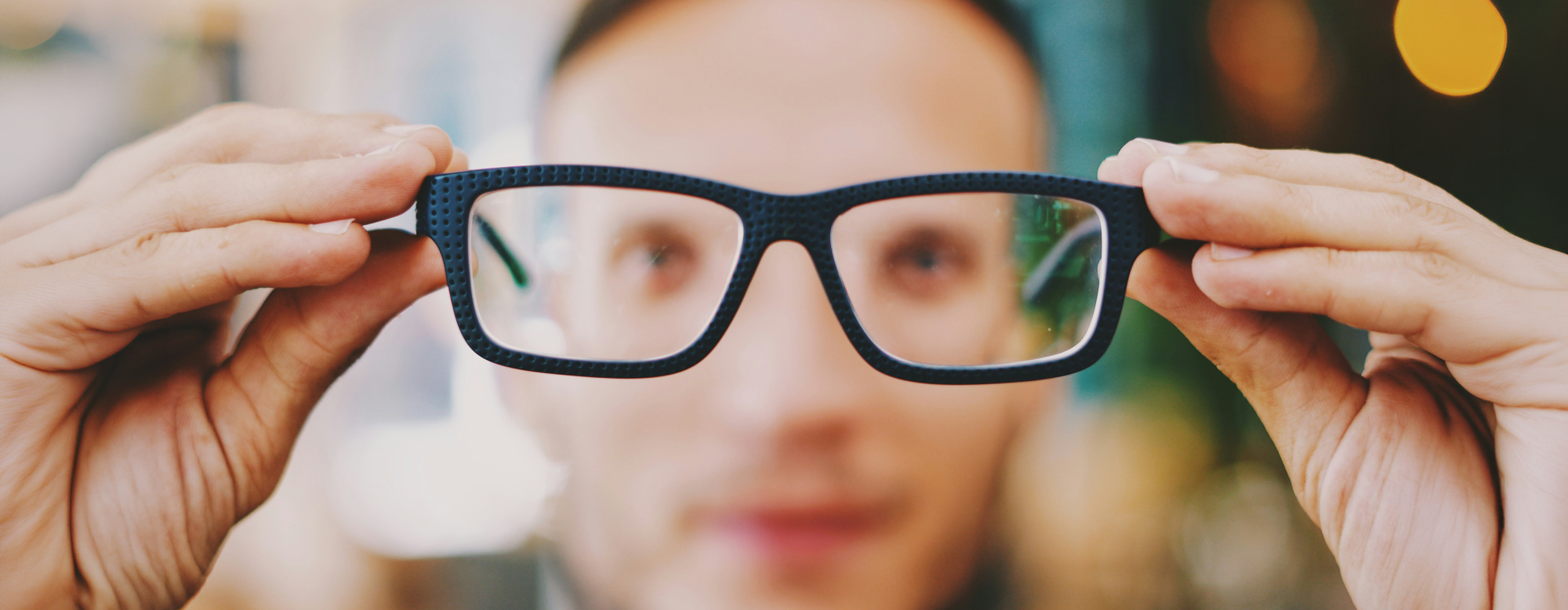 Opticien présentant une paire de lunettes à monture noire devant l'objectif dans un magasin d'optique