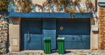 Maison de ville avec une porte et une porte de garage bleues et 2 poubelles vertes devant